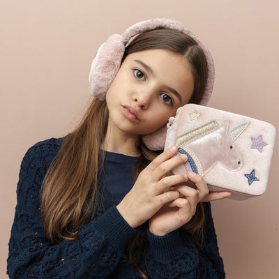 Dark haired girl pouting holding a blush pink velvet unicorn box bag- zip closure- cross body strap- glittery unicorn  and star detail and wearing matching pale pink fluffy unicorn design earmuffs
