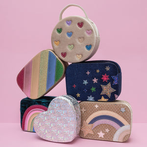 A stylish arrangement of silver holographic heart bag, navy velvet night sky bag, beige celestial star velvet bag, dazzle rainbow stripe bag, cream velvet jazzy heart bag, radiant teal rainbow velvet bag, displayed together, showcasing a coordinated collection with varying colours, textures, and designs.