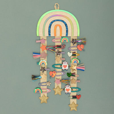 Bright metallic gold hanging rainbow with multicoloured stripes and gold ribbons with gold glitter padded star charms to the ends. Decorated with many different styles of hair clips including stars, hearts, rainbows and robots