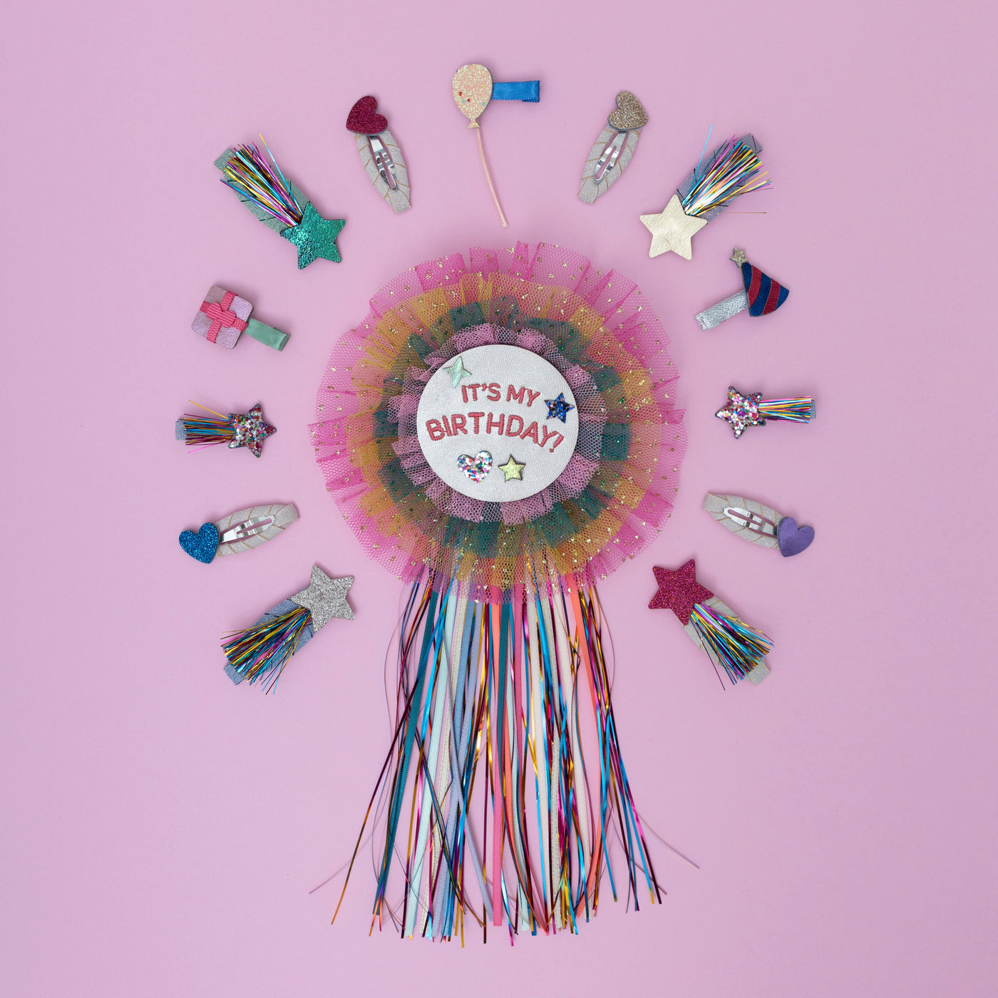 A vibrant rainbow birthday badge, bursting with a spectrum of bold colours, surrounded by a fun assortment of party-themed hair clips, perfect for adding a cheerful touch to any celebration