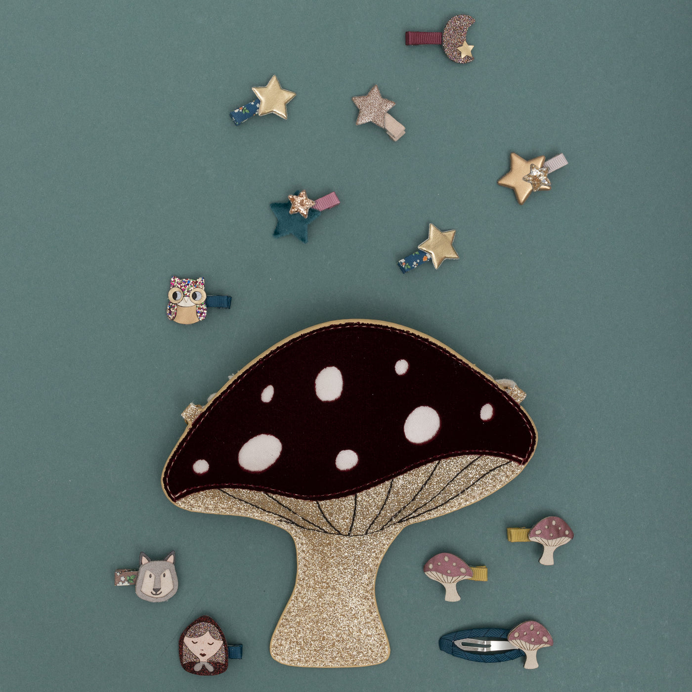 Velvet and glitter toadstool bag on a teal background surrounded by mini star and moon and toadstool hair clips