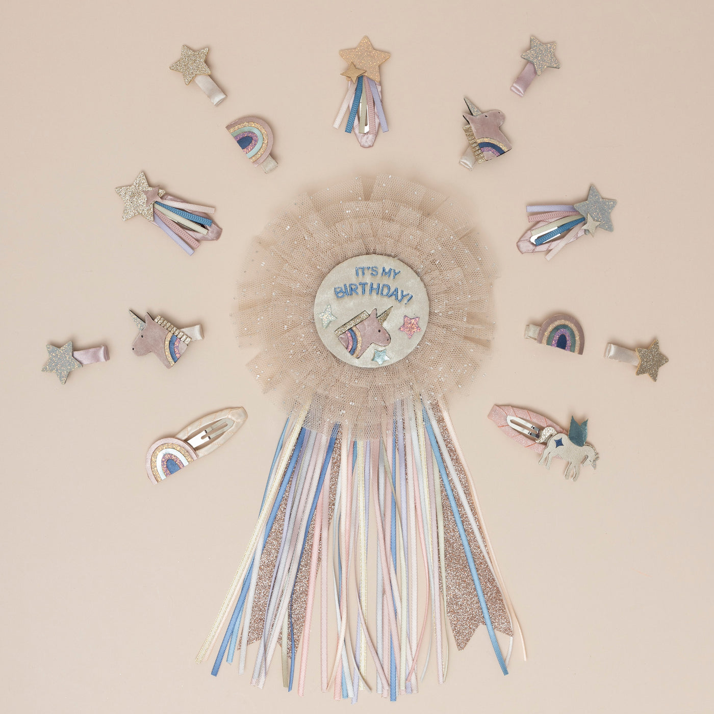 A magical unicorn birthday badge, featuring a sparkling unicorn design and encircled by glitter-speckled pink tulle, surrounded by an array of unicorn-themed hair clips, featuring glittery horns and manes, and whimsical stars, perfect for adding a fantastical touch to any celebration