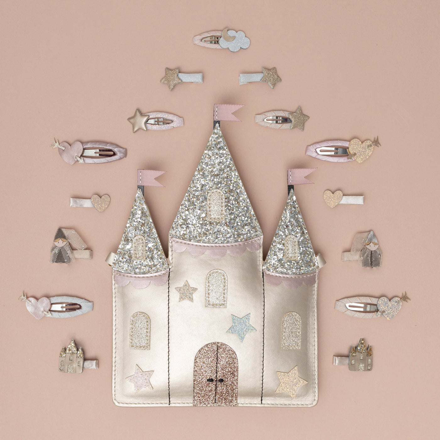 An enchanted gold castle bag, featuring glittery spires with pink flags and a cream cord crossbody strap, surrounded by a collection of princess and castle-themed hair clips