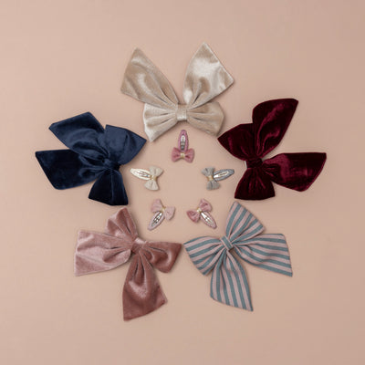 A circle of soft velvet oversized bows in beige, pink, deep red, striped, and navy, surrounding a collection of soft velvet mini bow clips, creating a charming and elegant arrangement with a mix of rich hues and textures
