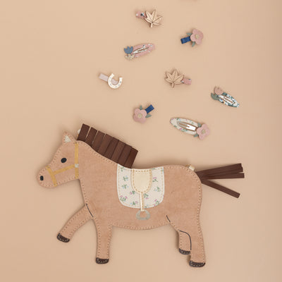 Sweet horsey handbag laid on a neutral background with floral mini hair clips above