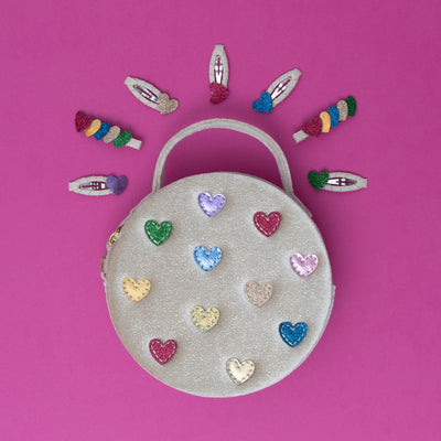 A cream velvet jazzy heart bag adorned with multi-coloured hearts, surrounded by a vibrant collection of brightly coloured heart-shaped hair clips