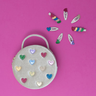 A cream velvet jazzy heart bag adorned with multi-coloured hearts, surrounded by a vibrant collection of brightly coloured heart-shaped hair clips