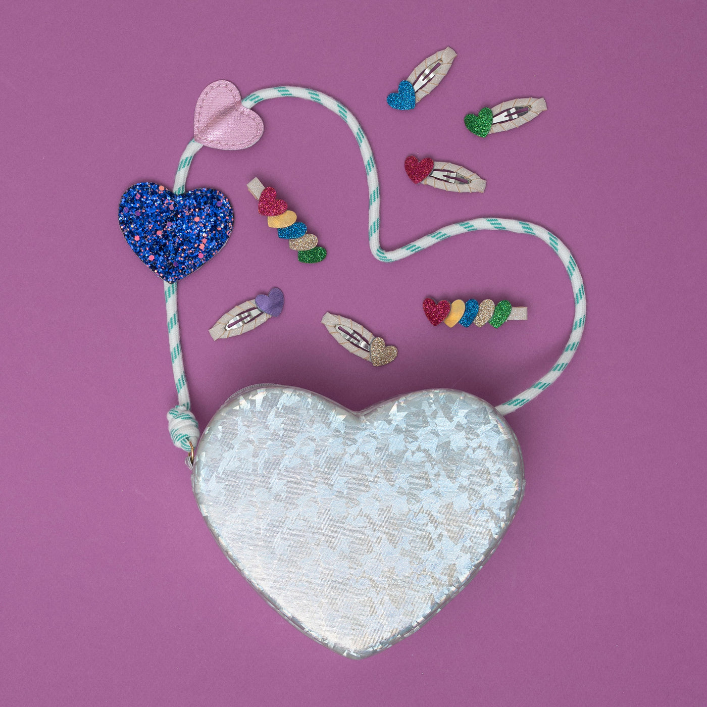 A silver holographic heart bag, shimmering with a reflective glow, surrounded by a collection of dazzling, heart-shaped hair accessories