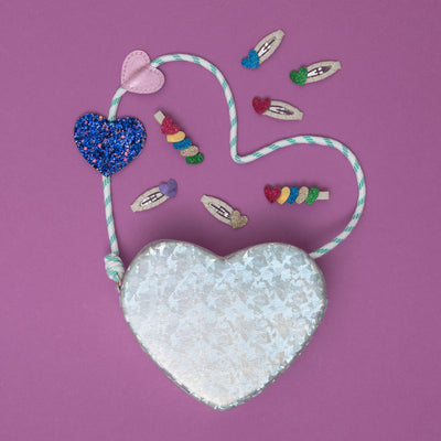 A silver holographic heart bag, shimmering with a reflective glow, surrounded by a collection of dazzling, heart-shaped hair accessories