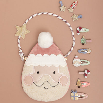 Fleece and velvet Santa handbag with cool cross body rope strap, surrounded by Christmas theme mini hair clips on a neutral background