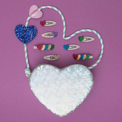 A silver holographic heart bag, shimmering with a reflective glow, surrounded by a collection of dazzling, heart-shaped hair accessories