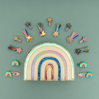 Beautiful metallic rainbow handbag laid on green background with shooting star hair clips and rainbows surrounding the bag