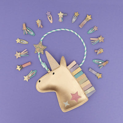 Metallic gold unicorn handbag for girls with colourful bungee cord strap, rainbow mane, on a purple background with assorted rocket and star hair clips around