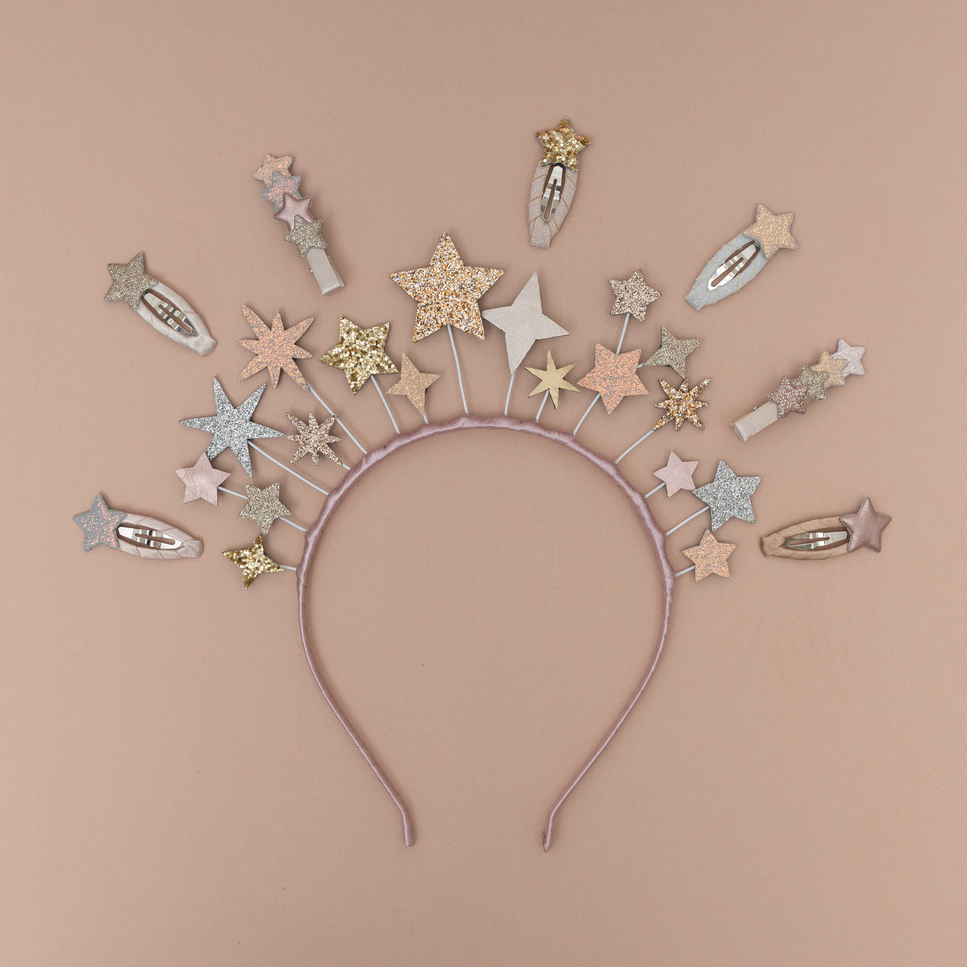 A magical star headdress, encircled by a collection of sparkling glitter star-themed hair clips, set against a soft peach background, creating a whimsical and enchanting display