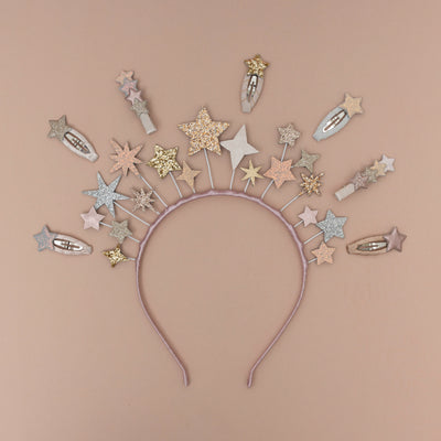 A magical star headdress, encircled by a collection of sparkling glitter star-themed hair clips, set against a soft peach background, creating a whimsical and enchanting display
