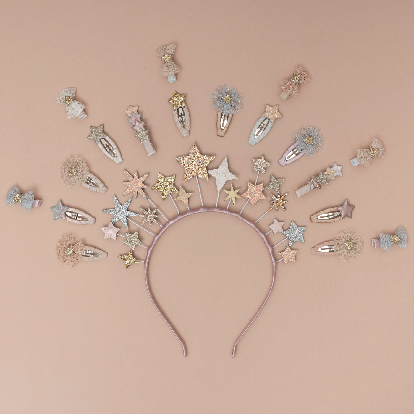 A magical star headdress, encircled by a collection of sparkling glitter star-themed hair clips, set against a soft peach background, creating a whimsical and enchanting display