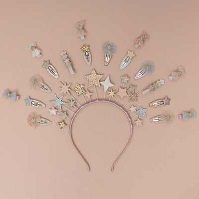 A magical star headdress, encircled by a collection of sparkling glitter star-themed hair clips, set against a soft peach background, creating a whimsical and enchanting display