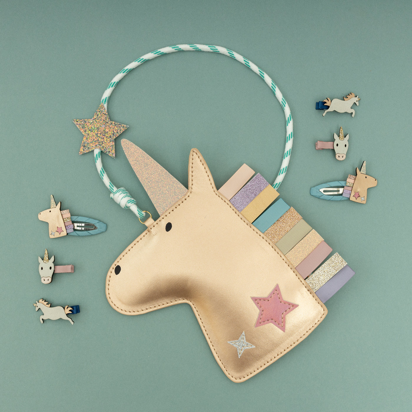 Matt metallic gold unicorn head shaped handbag with rainbow ribbon mane on green background