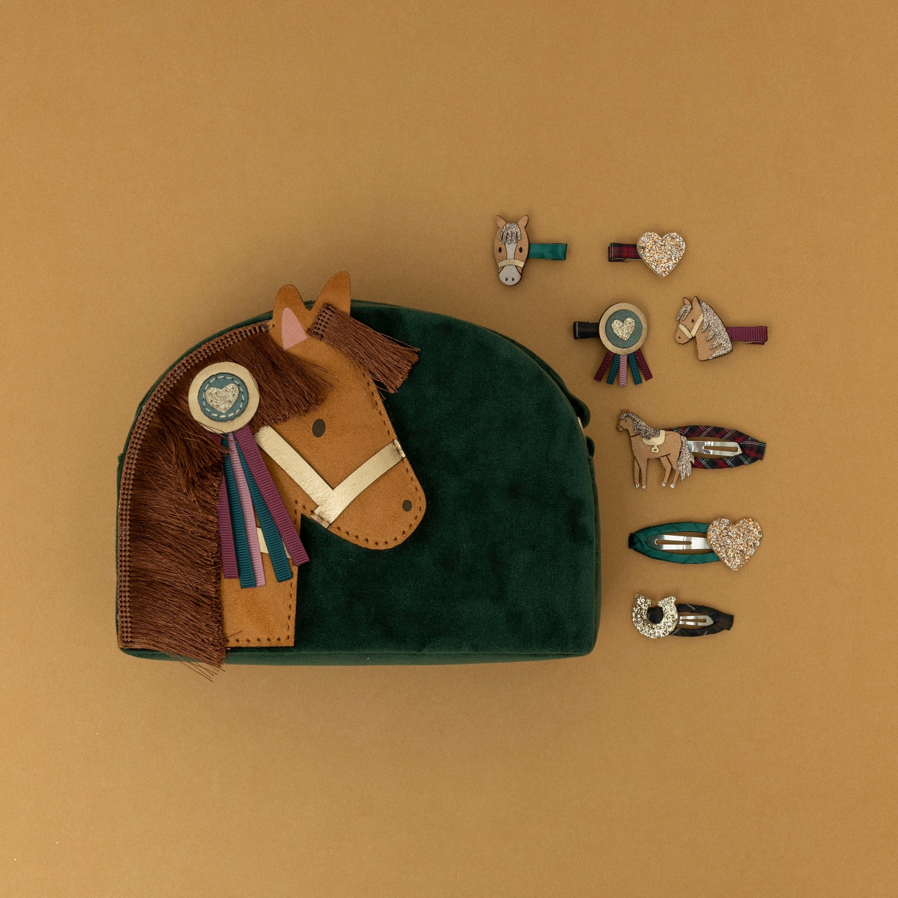 A green velvet pony pal bag with a matching green velvet strap, surrounded by an assortment of pony-themed hair clips, set against a warm golden yellow background