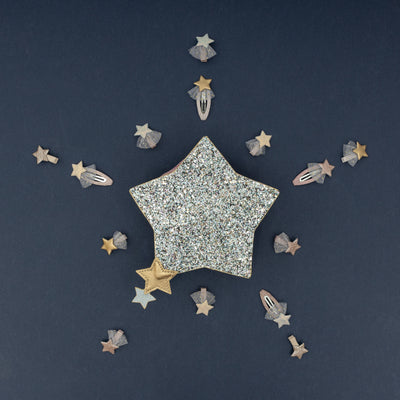 Silver glitter star shaped bag surrounded by little star hair clips on a navy background