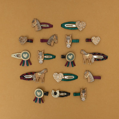 A collection of horse and pony-themed hair clips, featuring horseshoes and rosettes crafted from a mix of glitter and soft suedette fabrics, set against a warm golden yellow background