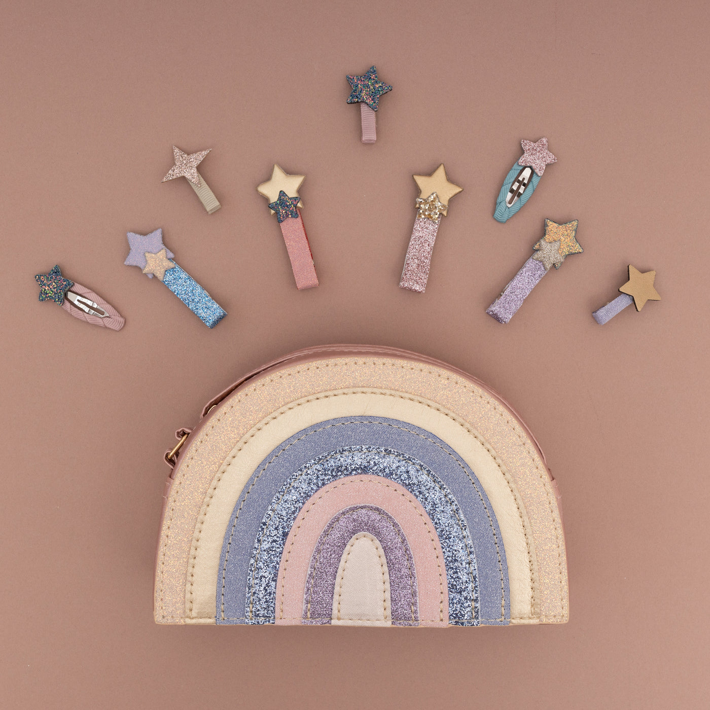 Pastel coloured glitter rainbow bag on pale brown background with a selection of glitter star hair clips placed above