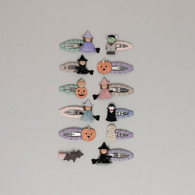 A selection of cute Halloween themed hair clips featuring Frankenstein, a mummy, an orange pumpkin, a bat, a witch on a broom, and Dracula, all set against a pale grey background