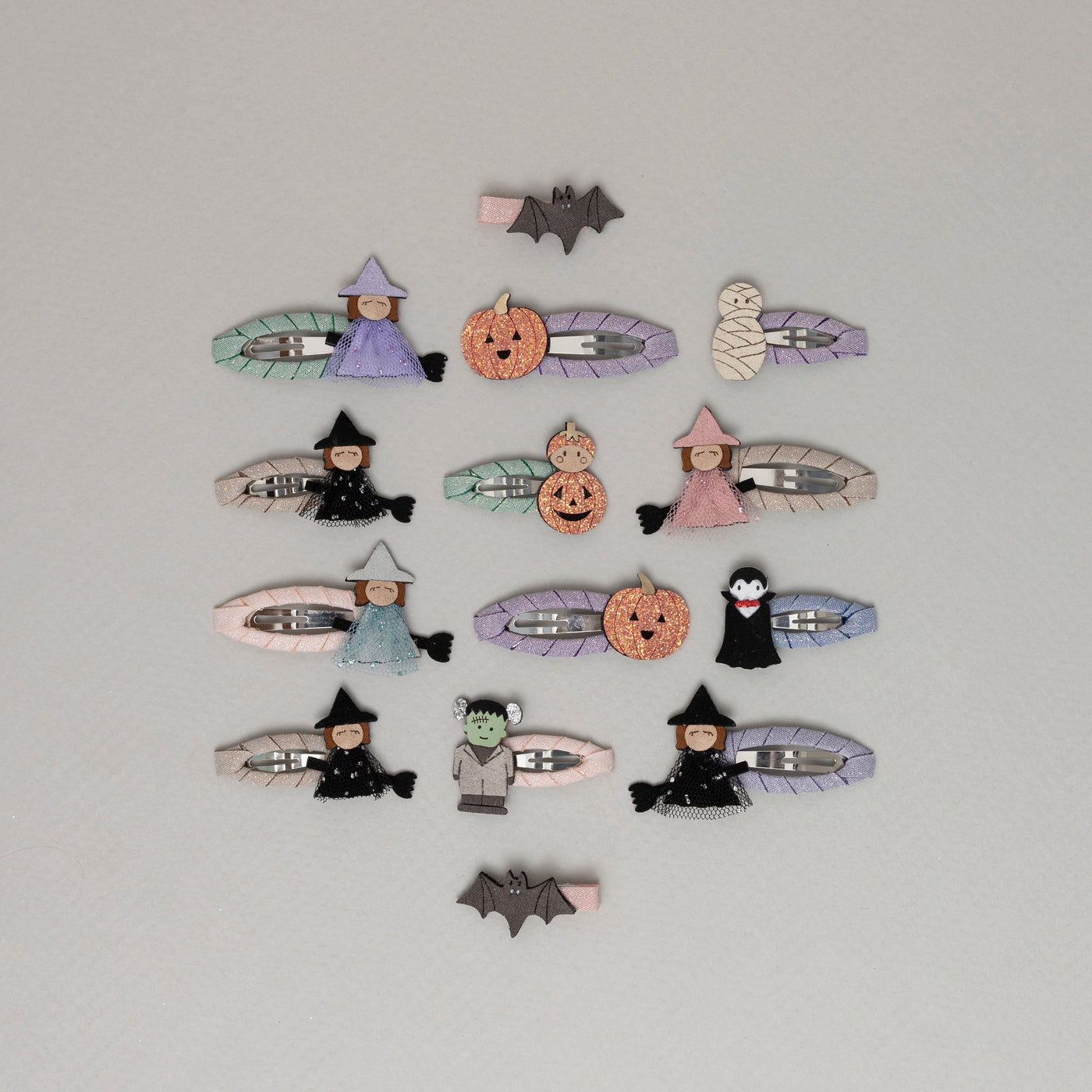 A selection of cute Halloween themed hair clips featuring Frankenstein, a mummy, an orange pumpkin, a bat, a witch on a broom, and Dracula, all set against a pale grey background