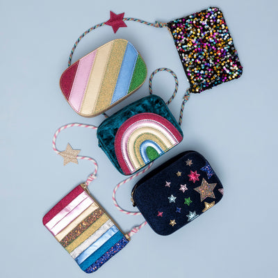 A stylish arrangement of navy velvet night sky bag, dazzle rainbow stripe bag, radiant teal rainbow velvet bag, dancing queen stripe bag and disco diva cross body bag displayed together, showcasing a coordinated collection with varying colours, textures, and designs.