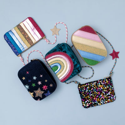 A stylish arrangement of navy velvet night sky bag, dazzle rainbow stripe bag, radiant teal rainbow velvet bag, dancing queen stripe bag and disco diva cross body bag displayed together, showcasing a coordinated collection with varying colours, textures, and designs