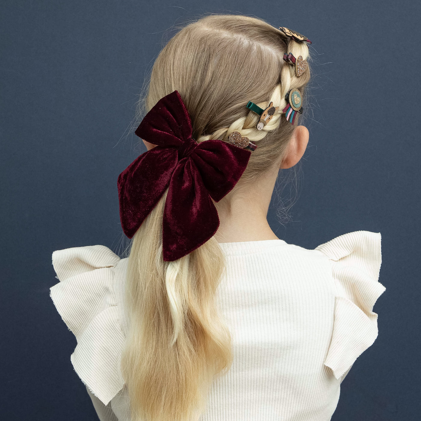 Blonde girl wearing pony pals mini clips on a dark blue background and Agnes bow clip