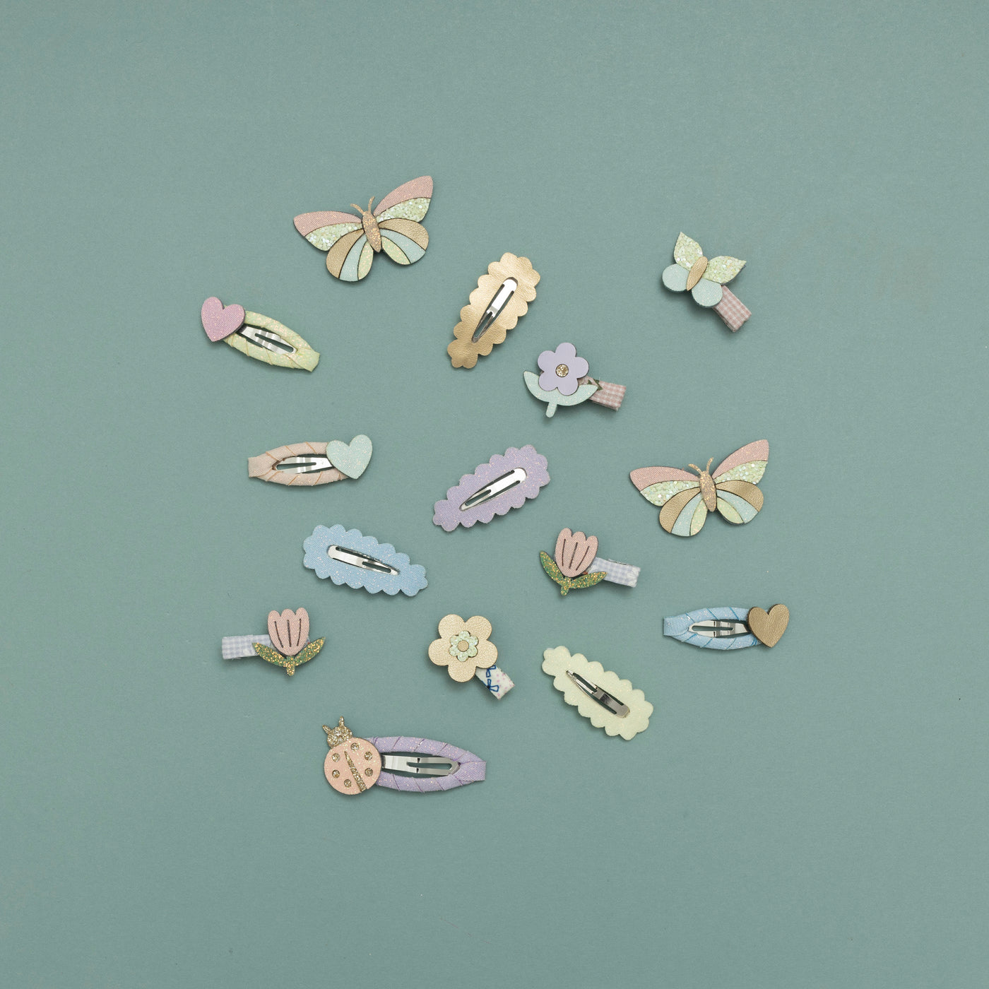 Selection of pastel coloured flower, ladybird, butterfly and heart hair clips arranged on a teal background