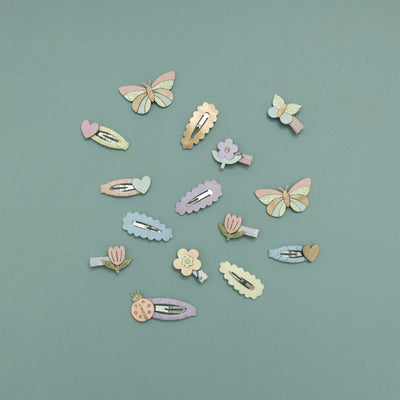 Selection of pastel coloured flower, ladybird, butterfly and heart hair clips arranged on a teal background