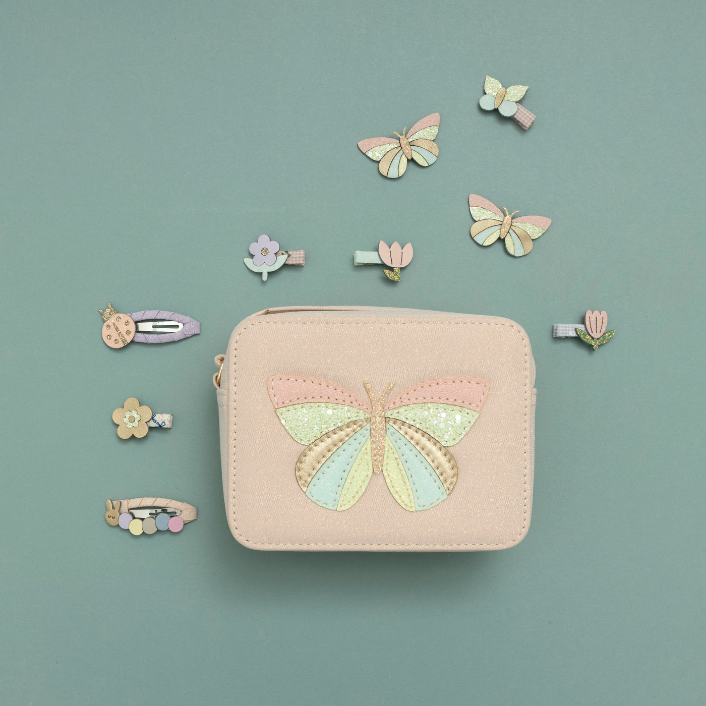 Glitter fabric handbag featuring delicate butterfly motif in glitter and pastel coloured fabrics on teal background with insect and flower pastel coloured hair clips surrounding the bag