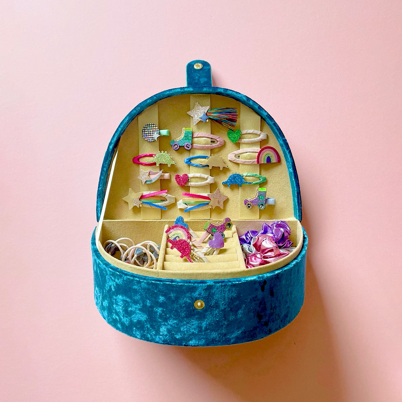 Bright rainbow jewellery box filled with colourful hair clips from Mimi & Lula against a pink background