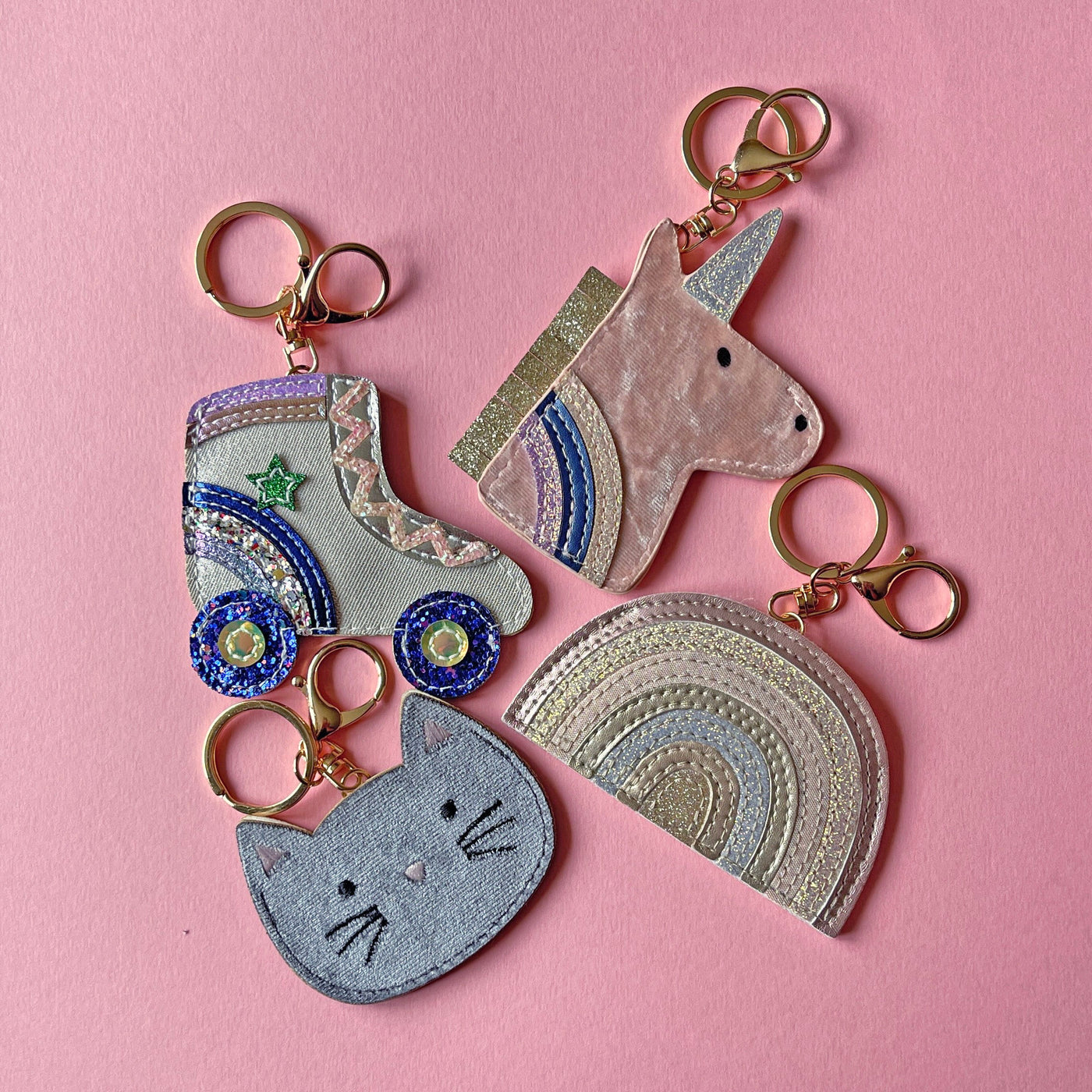 Three colorful keychains shaped like a cat, unicorn, and rainbow on a pink background