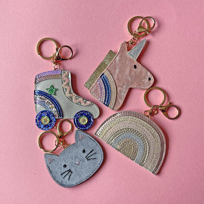 Three colorful keychains shaped like a cat, unicorn, and rainbow on a pink background