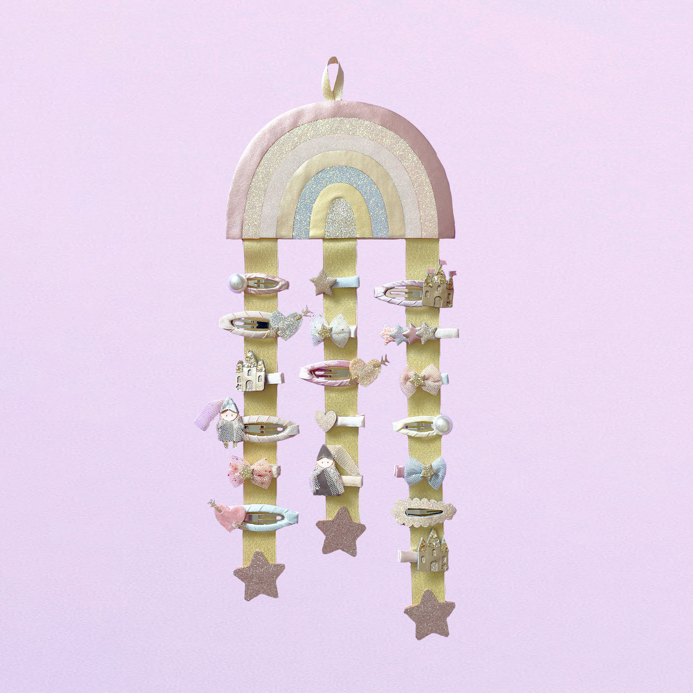 Pink rainbow wall hanger with hair clips attached against a pink background
