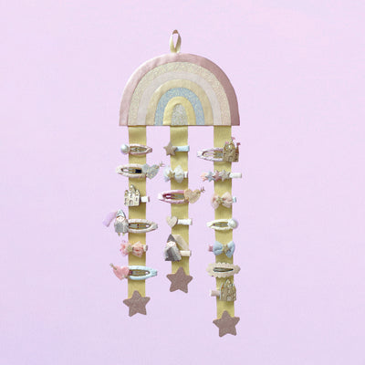 Pink rainbow wall hanger with hair clips attached against a pink background
