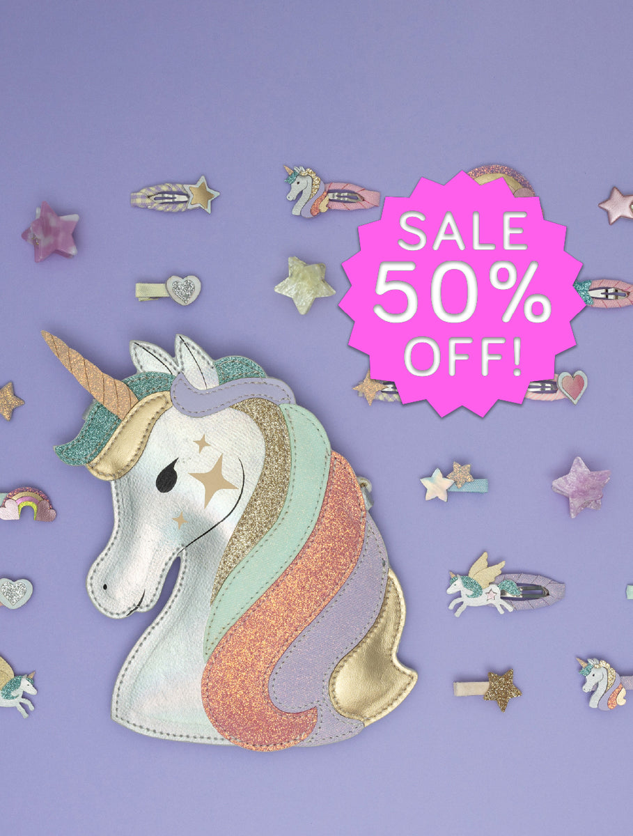 A pastel unicorn bag with a glittery rainbow mane and horn, displayed on a lavender background with scattered star and unicorn hair clips and a pink 'SALE 50% OFF!' badge.