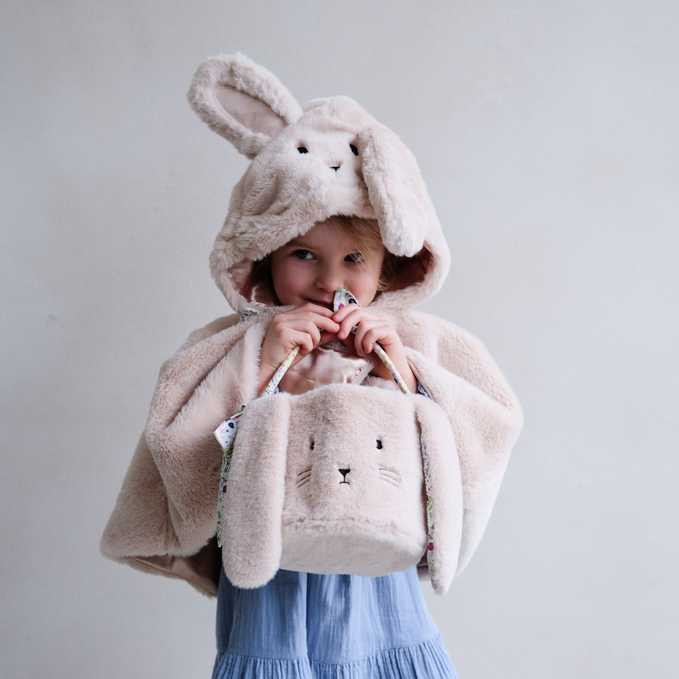 Little girl holding a fluffy bunny face Easter basket with floppy ears, wearing a fluffy bunny cape