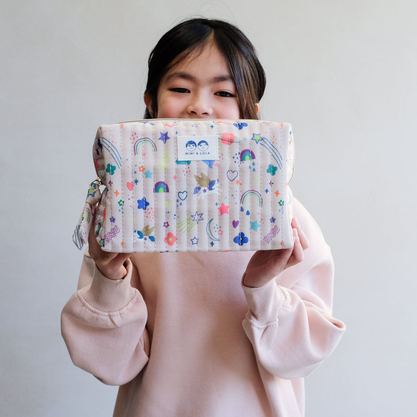 Little girl holding a rectangular wash bag in a brightly coloured, fun unicorn print fabric