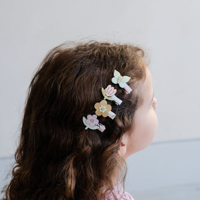 Little girl wearing a row of four mini pastel coloured flower and butterfly hair clips to the side