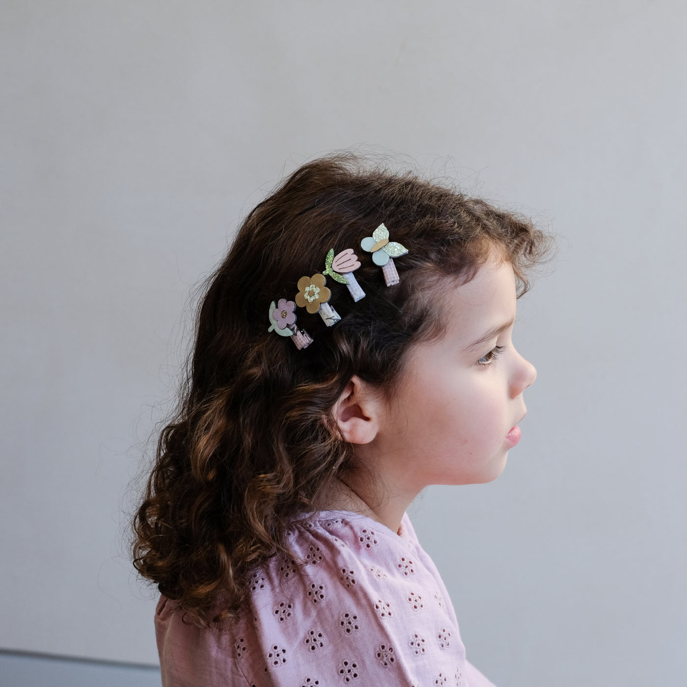 Little girl wearing a row of four mini pastel coloured flower and butterfly hair clips to the side