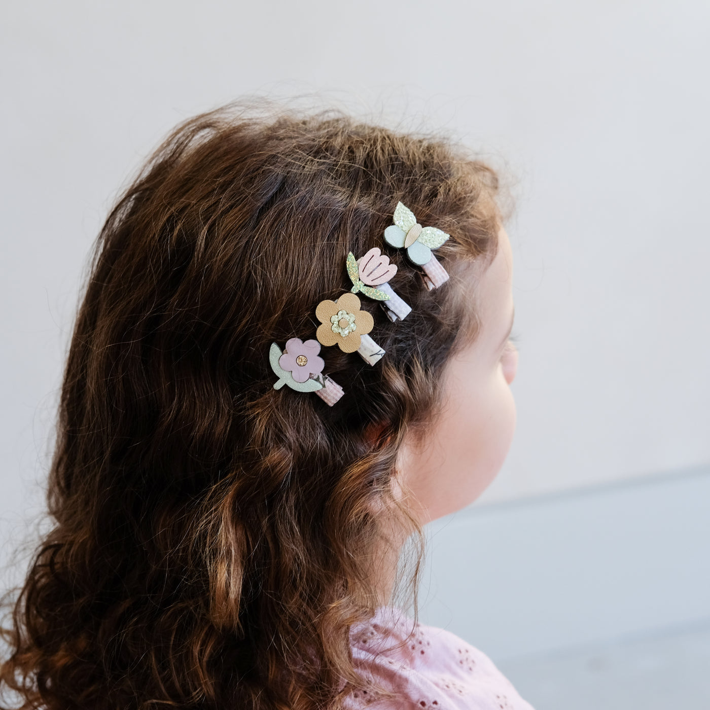 Little girl wearing a row of four mini pastel coloured flower and butterfly hair clips to the side