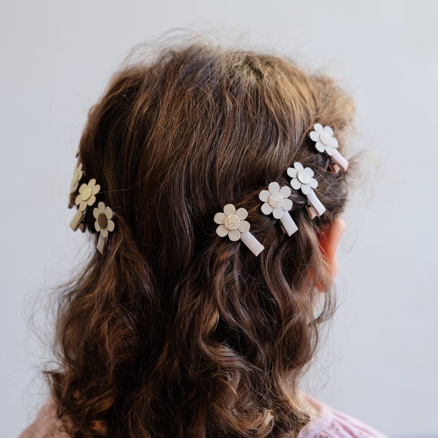 Eight mini hair clips in pink and neutral glitter fabrics featuring gold and cream glitter daisy heads worn to either side of the hair