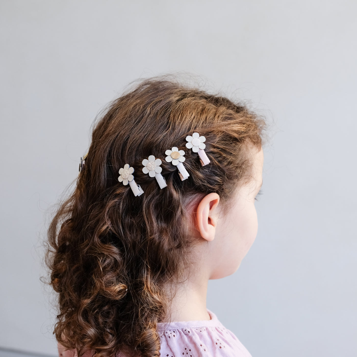 Row of four mini daisy hair clips worn to the side