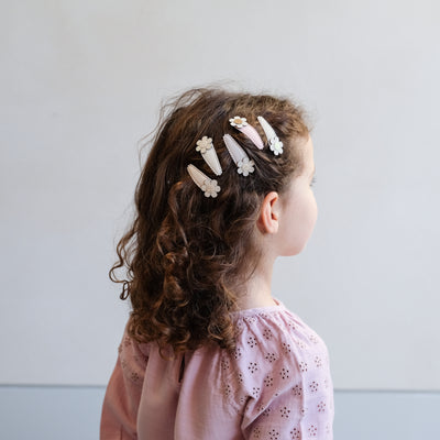 Little girl wearing five glitter hair clips featuring cream and gold fabric daisies to the side