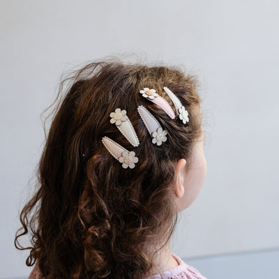 Little girl wearing five glitter hair clips featuring cream and gold fabric daisies to the side