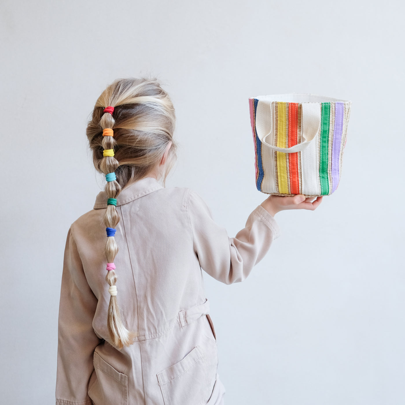 girl with rainbow bobble pony hair style using Mimi & Lula rainbow towelling ponies holding a rainbow straw bag